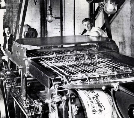 Two pressmen are working in an old fashion pressroom with an old stop-the-presses type press.