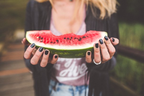 A woman's hands holding a slice of watermelon with some bites taken from it.