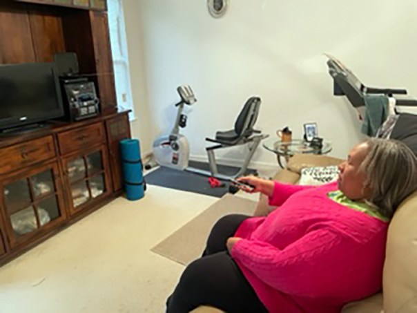 Empish watching TV. She is sitting on sofa pointing remote control at TV.
