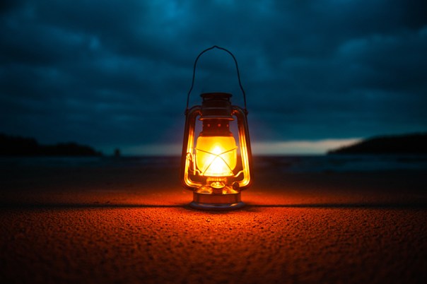 A gaslight on the ground with an orange glow. It is outside at night with dark clouds above.
