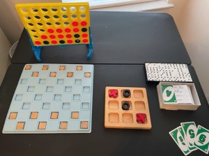 A display of various accessible games on a table. Games include Connect Four, Braille Uno cards and Braille Dominos.