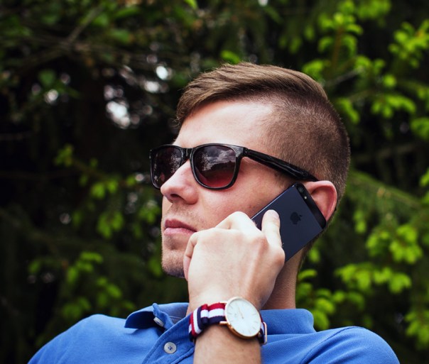 A man is outdoors talking on an iphone. The back of the phone is showing so the iphone logo is visible.