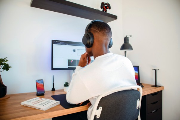 A teenage boy wearing headphones. He is sitting in front of his desktop computer and studying.
